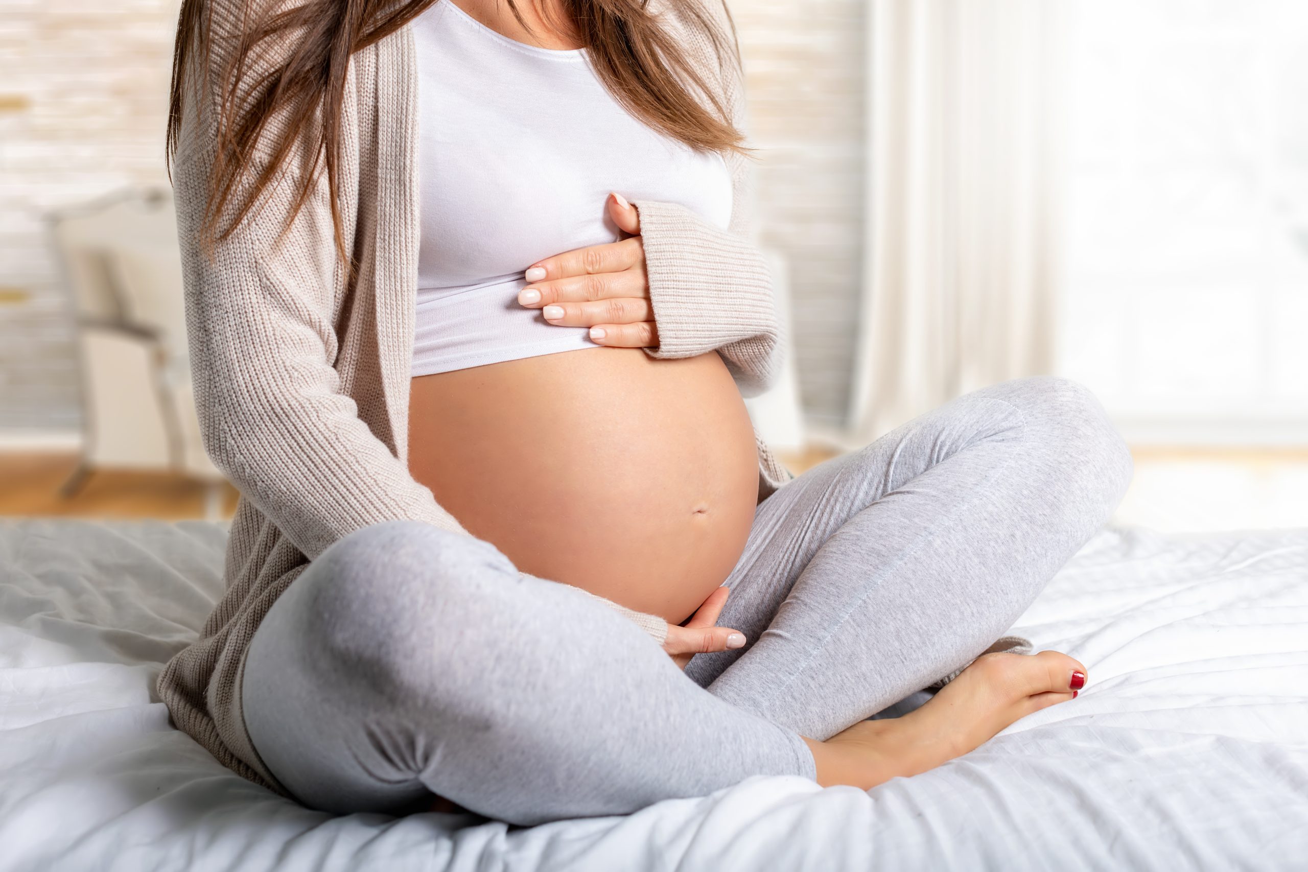 Midsection Of Pregnant Woman Sitting On Bed At Home