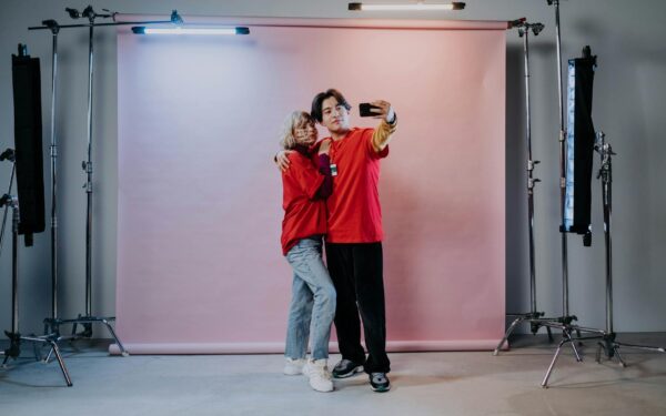 A couple poses for a selfie in a professional studio setting, surrounded by lighting equipment.