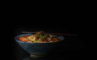 Close-up of a flavorful Asian noodle soup with meat and vegetables, served in a patterned bowl on a dark background.
