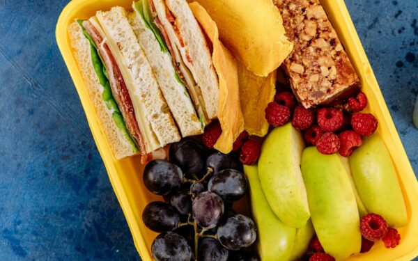 Vibrant lunchbox containing a sandwich, fresh fruits, and a snack bar, ideal for healthy meals.