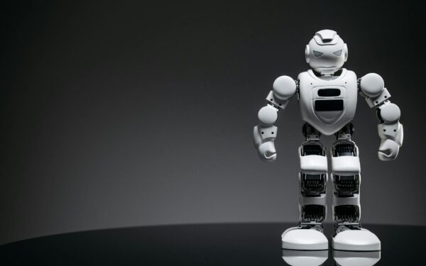Close-up of a white toy robot on a reflective surface with dark background.