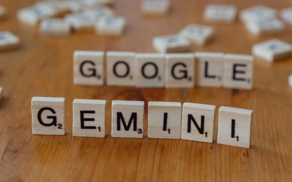 Scrabble tiles spelling out Google and Gemini on a wooden table, focusing on AI concepts.