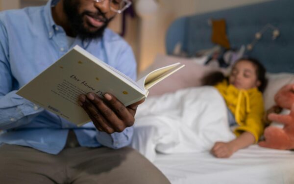 A father reading a bedtime story to his daughter, who is lying in bed, creating a warm and cozy atmosphere.