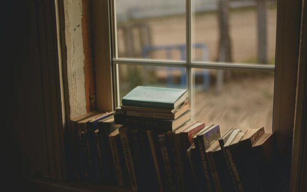 A collection of books stacked by a rustic window, evoking a warm, serene atmosphere.