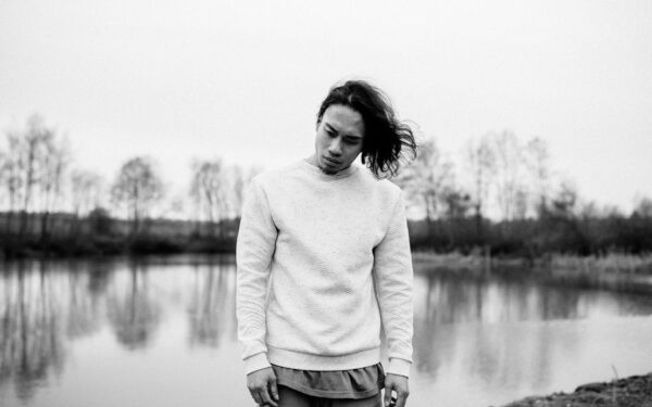 A thoughtful man stands by a serene lake, reflecting on life in a natural setting.