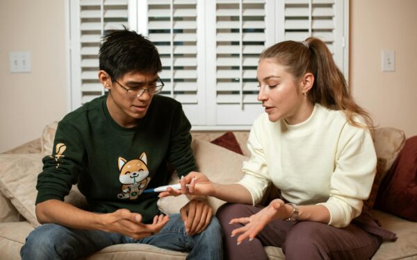A couple sitting on a sofa discussing the result of a home pregnancy test, showing diverse emotional reactions.