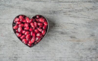 Delicious and juicy pomegranate seeds in a heart-shaped bowl on a wooden table.