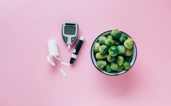 Top view of a glucometer and fresh Brussels sprouts on a pink background promoting health.
