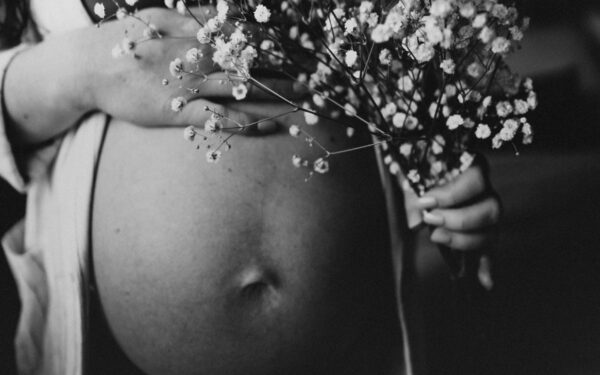 Artistic black and white photo of a pregnant woman holding flowers against her belly.