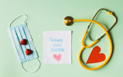 Flat lay of thank you note for doctors with stethoscope, mask, and hearts on green background.