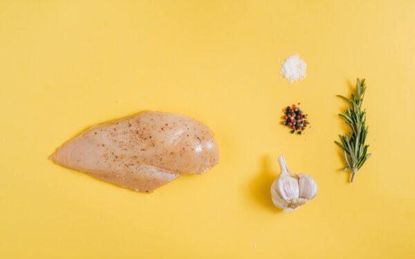 Chicken breast with garlic, rosemary, and spices on a yellow background.