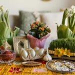 A vibrant arrangement of Nowruz haft-seen elements featuring greenery, flowers, and traditional items.
