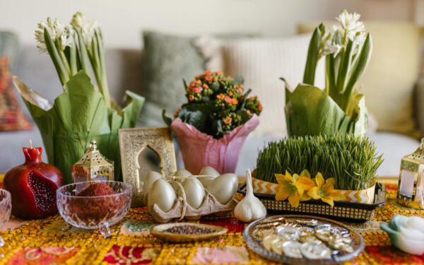 A vibrant arrangement of Nowruz haft-seen elements featuring greenery, flowers, and traditional items.