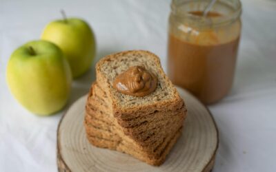 Stack of whole grain bread with peanut butter, accompanied by apples and a jar of smooth peanut butter.