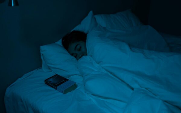 A woman peacefully sleeping with a book under blue night lighting, showcasing a cozy bedtime atmosphere.
