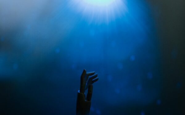 Silhouette of a robotic hand reaching towards glowing blue light in a futuristic setting.