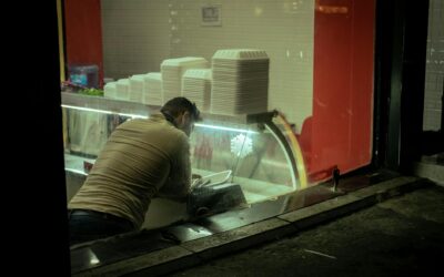 A man arranging containers in a takeaway restaurant, seen through a window.