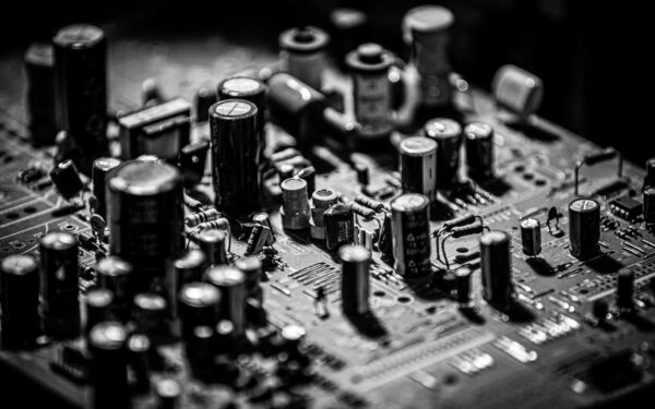 Grayscale close-up of electronic circuit board with capacitors and transistors.