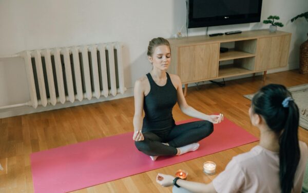 Two women meditating on a yoga mat indoors, practicing mindfulness and relaxation.