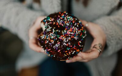 Close-up of a chocolate doughnut with colorful sprinkles held in hands, perfect for sweet treat lovers.