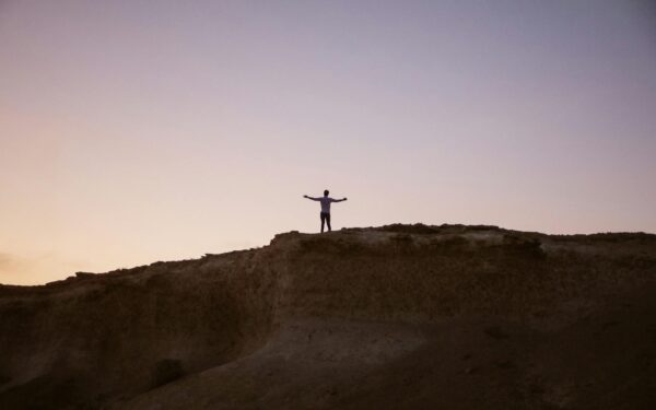 Silhouette of a person standing on a hill with arms spread at twilight, symbolizing freedom and tranquility.