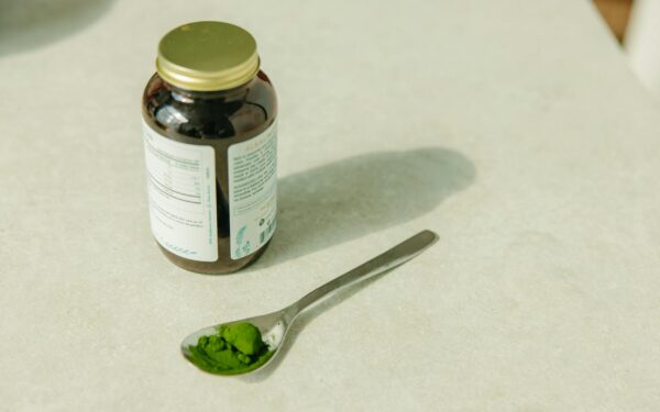 Close-up of a jar and a spoon with green powder, ideal for healthcare and wellness themes.