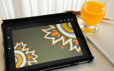 A tablet displaying mandala artwork beside a glass of orange juice on a table.