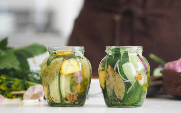 Two glass jars filled with homemade pickled cucumbers and herbs on a white kitchen surface.