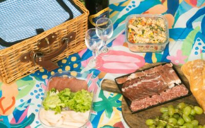 Colorful picnic arrangement featuring charcuterie, grapes, pasta salad, and a wicker basket.