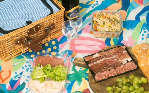 Colorful picnic arrangement featuring charcuterie, grapes, pasta salad, and a wicker basket.