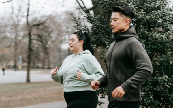 Side view of overweight woman in sportswear running with Asian trainer in city park in daytime