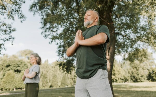 Elderly couple meditating in a peaceful park setting, promoting a healthy lifestyle.