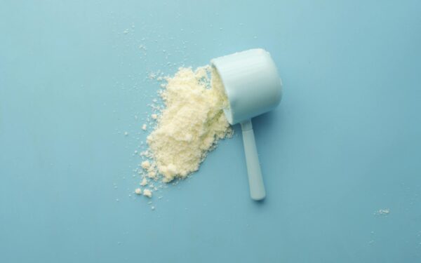 White powder spilled from a scoop on bright blue background. Clean and minimalistic food photo.
