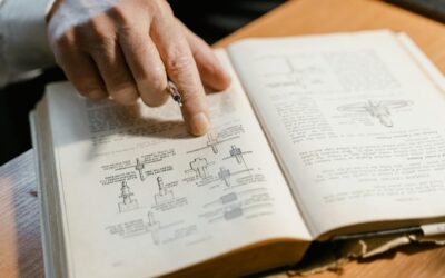 A hand points to a diagram in an open book focused on engineering concepts, highlighting learning.