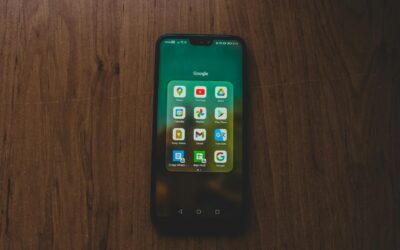 A smartphone showcasing various Google apps on a wooden table.