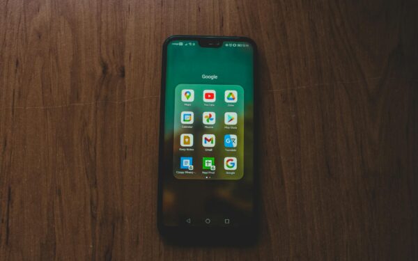 A smartphone showcasing various Google apps on a wooden table.