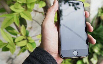 A hand holding a smartphone against a background of green leaves, capturing a modern lifestyle moment.