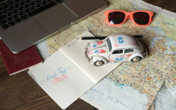 Flat lay of a road trip plan featuring maps, passport, toy car, and travel essentials.
