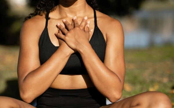 A woman in activewear practices mindfulness meditation outdoors, hands on chest.