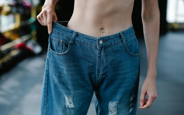 A woman showcases significant weight loss results confidently wearing loose jeans.