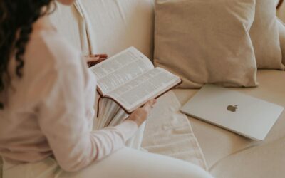 Woman reading a book on a cozy sofa with a laptop nearby. Ideal for lifestyle and relaxation themes.