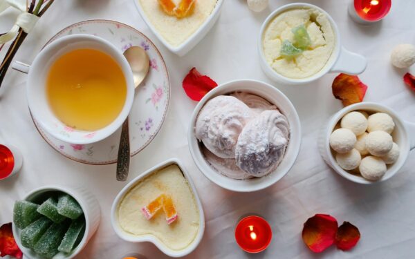 A flat lay of desserts and tea with candles and petals on a white background, creating a cozy ambiance.