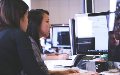 Two women working together on code at a computer in a modern office setting.