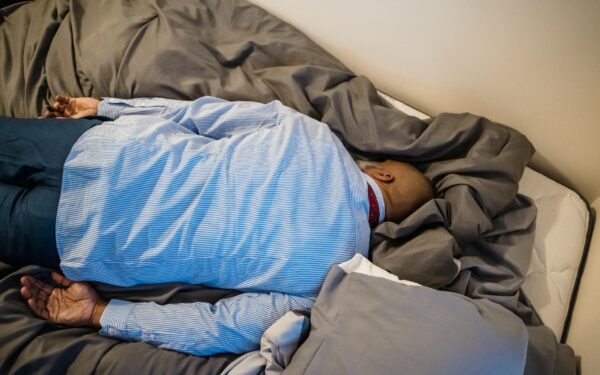 A man in formal attire rests face down on a bed, conveying exhaustion and fatigue.