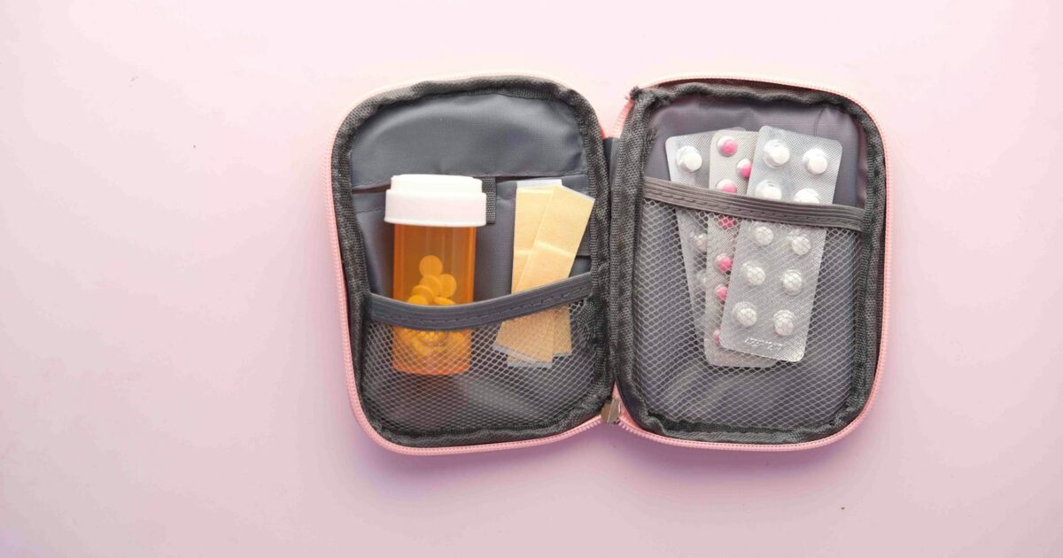 Open first aid kit with pill bottle, blister packs, and band-aids on a pastel background.