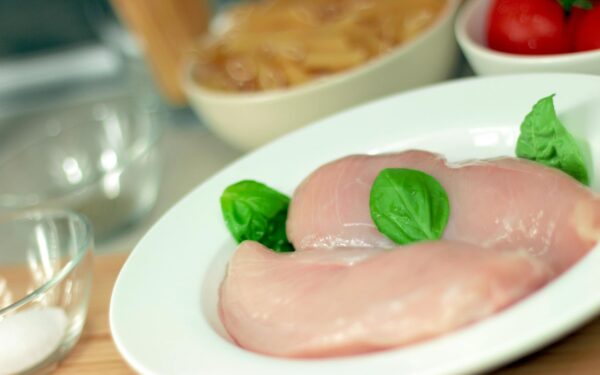 Close-up of raw chicken breasts on a plate with basil leaves, ideal for culinary themes.