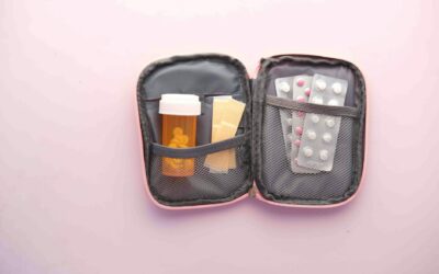 Open first aid kit with pill bottle, blister packs, and band-aids on a pastel background.