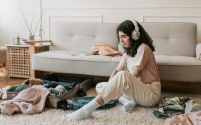 Young woman with headphones packing suitcase in a cozy living room.